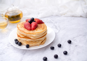 Stack of pancakes with topping, strawberry and blueberry.Placed in a white plate on a marble table and copy space.Eat with tea in the glass.