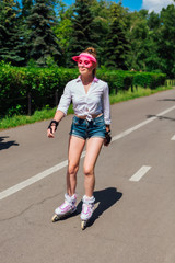 Portrait of an emotional girl in a pink cap visor and protective gloves for rollerblades and skateboarding riding on rollerblades on the road.