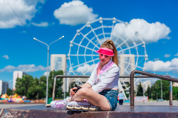 Portrait of an emotional girl in a pink cap visor wearing protective gloves and rollerblades...