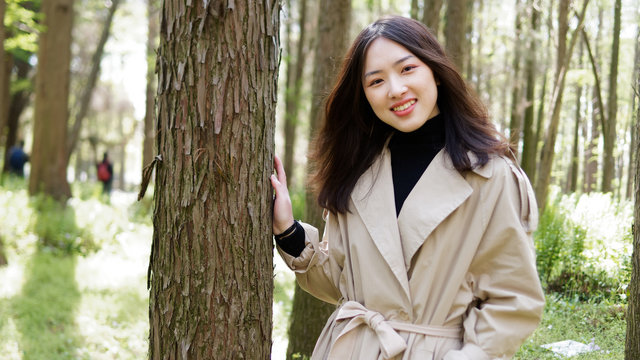 Beautiful young brunette woman posing and smiling in forest park. Outdoor fashion portrait of glamour Chinese stylish lady with black long hair. Emotions, people, beauty and lifestyle concept.