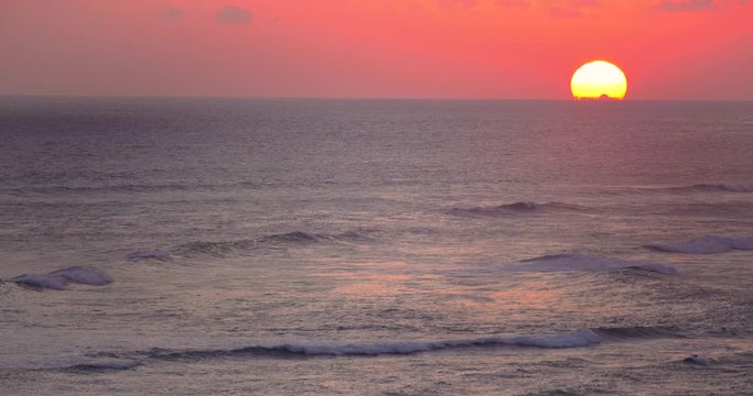 Calm and relaxing view of golden sun setting below horizon and slow moving waves, Indonesia