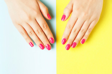 Female hands with pink manicure on yellow and blue background