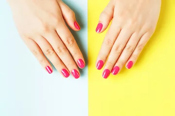 Female hands with pink manicure on yellow and blue background