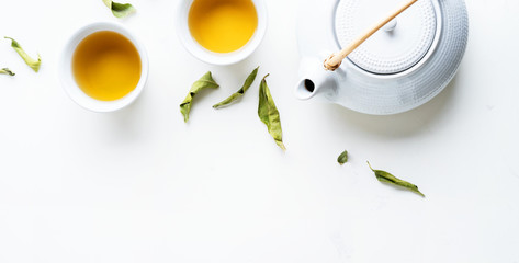 Asian tea concept, two white cups of tea and teapot surrounded with green tea dry leaves view from...