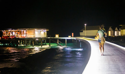 Woman walk on boardwalk at night.