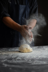 chef in the kitchen, male hands knead the dough, clap hands, a cloud of flour - obrazy, fototapety, plakaty