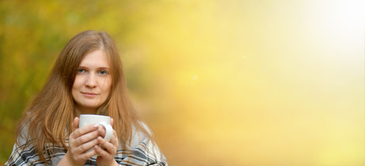 Banner. Autumn.  Cold girl. Portrait of a girl who holds a Cup of hot tea, wrapped in a blanket, looking at the camera in the autumn forest . Autumn background