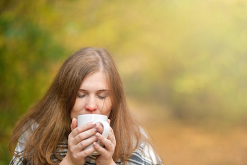  Autumn.  Cold girl. Portrait of a girl who holds a Cup of hot tea, wrapped in a blanket, looking at the camera in the autumn forest . Autumn background