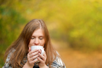  Autumn.  Cold girl. Portrait of a girl who holds a Cup of hot tea, wrapped in a blanket, looking at the camera in the autumn forest . Autumn background