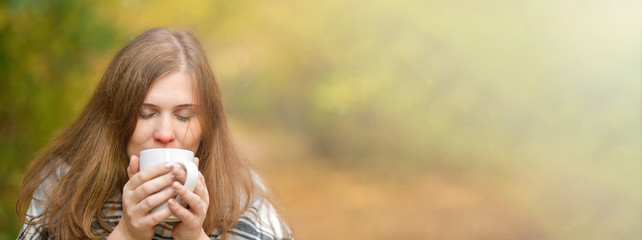 Banner.  Autumn.  Cold girl. Portrait of a girl who holds a Cup of hot tea, wrapped in a blanket, looking at the camera in the autumn forest . Autumn background