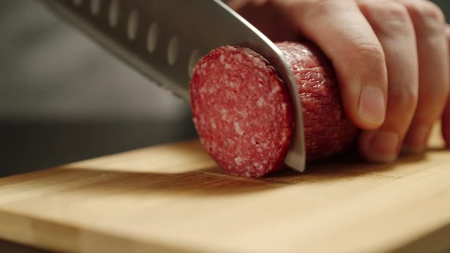 Man Cutting Salami Sausage On Wooden Board