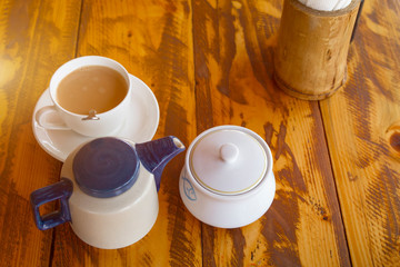 Traditional indian tea set with masala chai. Composition from teapot, sugarbowl and cup on wooden table. Top veiw. Sunlight toned.
