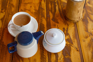 Traditional indian tea set with masala chai on wooden background. Composition from teapot, sugarbowl and cup on table. Top veiw.
