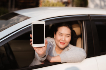 Attractive young woman in auto shows smartphone with blank screen.