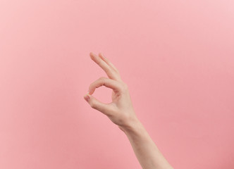 Woman hand shows ok symbol on pink pastel background with copy space