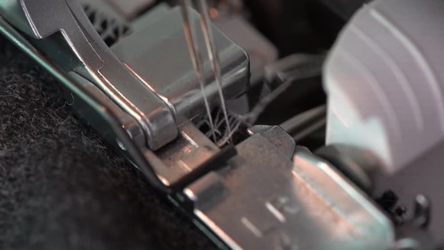 Overlock Sewing Machine. Close up stitches in slow motion. Machine serging the edges of fabric. Presser feet