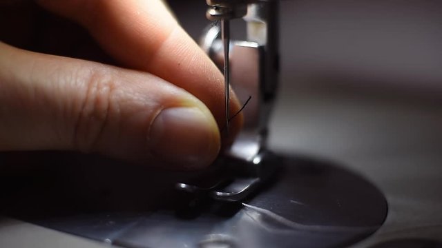 Close up of presser foot and needle of sewing machine, lighting with built-in hardware lamp. Accurate cropped fingers pulling black thread through needle before sewing process. Blurred background. POV