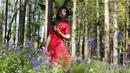 Naklejka premium Portrait of beautiful young brunette woman in red dress looking away in forest park in sunny windy summer day. Outdoor fashion portrait of glamour Chinese stylish lady. Beauty, lifestyle Concept.