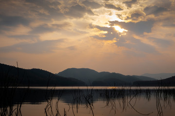 Obraz premium Landscape of the sun shining through cloudy sky over the lake with crystal clear water and mountains at a national park during sunrise. 
