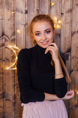 Fototapeta premium Beautiful young woman dressed in a sweater and skirt standing next to the wooden wall with star and moon lights
