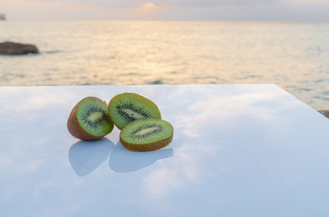 Tropical snack - Green and hairy sliced kiwi on a white table - Sunset on the sea bottom of the photo