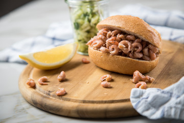Nordseekrabben Brötchen als Fischbrötchen mit Gurkensalat und Zitrone auf Holz Brett und Marmor...