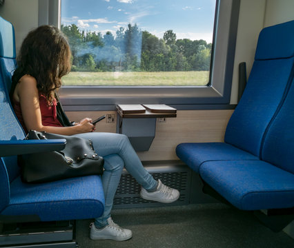 Ragazza con il cellulare in mano, seduta in un vagone del treno che messaggia e chatta con amici e famigliari