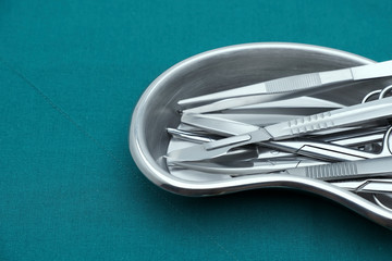 Basic surgical instrument scalpel forceps tweezers scissors in emesis or plus basin  on surgical green drape fabric