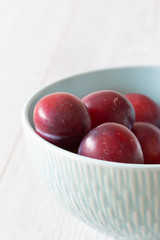 British organic plums, freshly picked, in a pastel green bowl dish. Grey wood background
