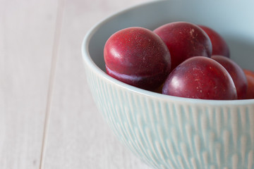 British organic plums, freshly picked, in a pastel green bowl dish. Grey wood background