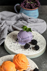 Berry ice cream. Decorated with blackberries and mint leaves. Ceramic plate. Gray concrete background.