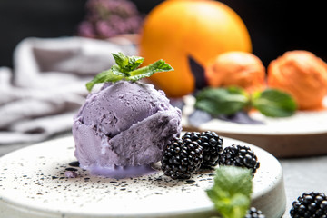 Berry ice cream. Decorated with blackberries and mint leaves. Ceramic plate. Gray concrete background.