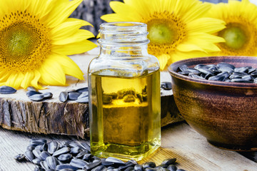 Sunflowers and seeds on a wooden background near sunflower oil in a glass jar. Healthy foods and fats.