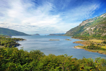 Naklejka na ściany i meble Panoramic view of Tierra del Fuego National Park, showing small islands surrounded by green vegetation and water, against a blue sky.