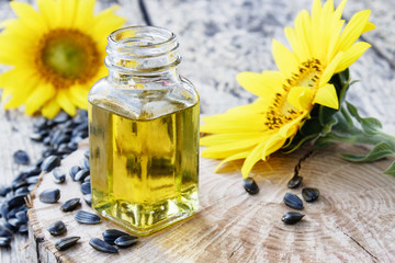 Organic sunflower oil in a glass jar with seeds and fresh flowers on a wooden background. Healthy foods and fats.