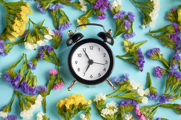 Alarm clock with colored flowers on blue background composition.