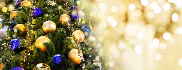 Obraz na płótnie Canvas Christmas tree decorated with Golden and blue balls toys on a blurred, sparkling and fabulous fairy background with beautiful bokeh, copy space, banner format.