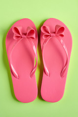 Pink rubber slippers on green background composition.