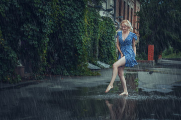 Young blonde woman in a dress frolics through puddles in the summer rain.