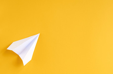 White paper plane on yellow background composition.