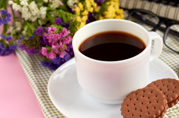 Coffee cup with cookies, alarm clock, flowers, mascara, on pink background composition.