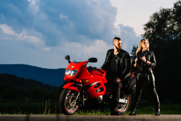 Fototapeta na wymiar man and woman bikers in leather jackets with sports motor bike on the road in the evening