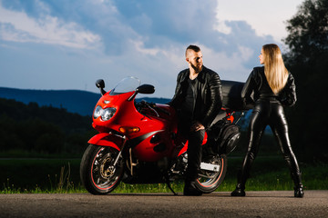 Fototapeta na wymiar man and woman bikers in leather jackets with sports motor bike on the road in the evening