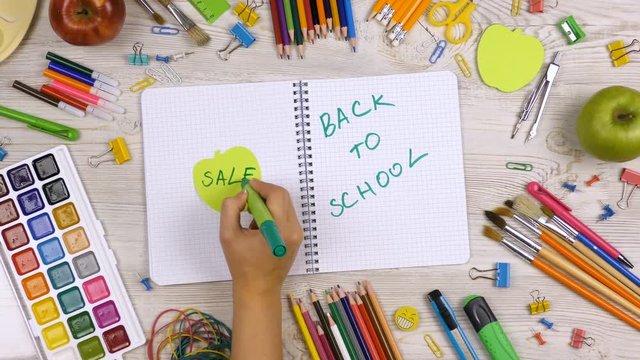 Back to school sale background with school supplies on the table. Girl writes in a notebook word sale.