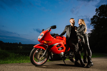 Fototapeta na wymiar Cool biker couple in leather jackets sitting on red sports bike outdoors