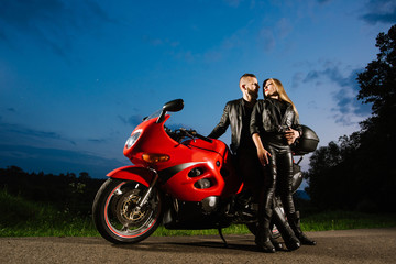 Obraz na płótnie Canvas Cool biker couple in leather jackets sitting on red sports bike outdoors