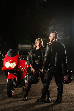 man and woman bikers in leather jackets with sports motor bike on the road in the evening