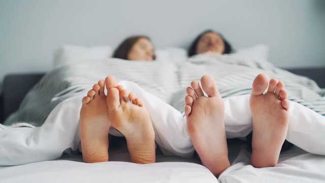 Girl and guy couple are napping in bed together lying under white blanket barefoot relaxing in apartment. People, relaxation and relationship concept.