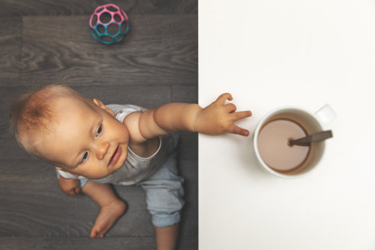 child burn and scald injury concept - little boy reaching for hot drink mug on the table