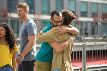 Happy close male friends hugging each other outside. Men meeting on outdoor building terrace and...